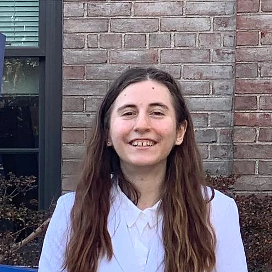 Headshot of Lillian Riggs, smiling in a white suit on the Hofstra University campus