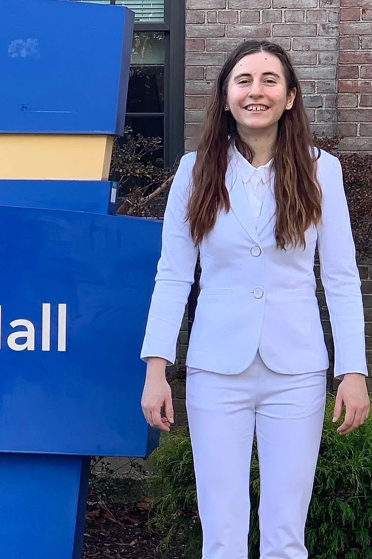 Lillian Riggs in a white suit beside the Hofstra University Barnard Hall sign