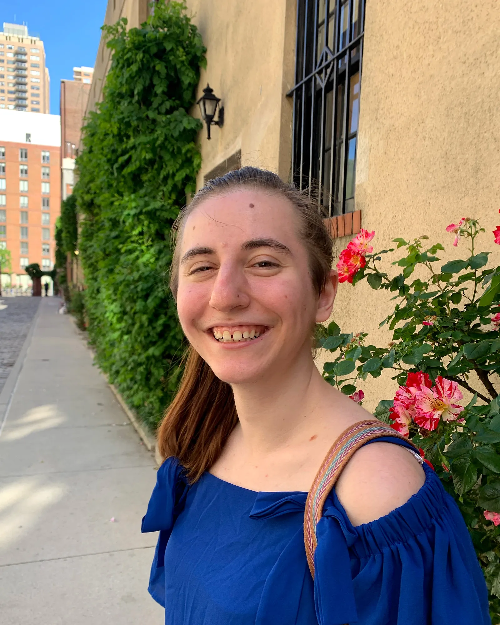 Lillian Riggs smiling on a city street beside climbing roses